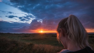 Uma mulher num campo com o pôr do sol à distância.