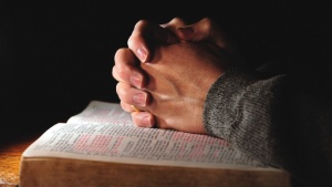 Mãos entrelaçadas em cima de uma Bíblia aberta.