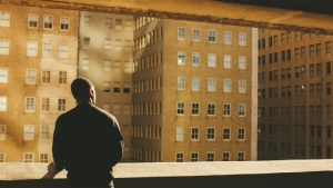Uma pessoa olhando por cima duma parede para edifícios numa cidade.