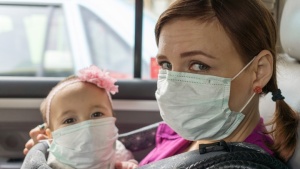 Uma mulher e uma criança pequena usando máscaras, sentados num carro.