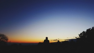 Uma pessoa sentada no topo da colina olhando para a extensão do céu noturno.