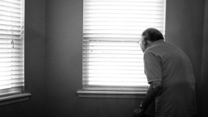 Um homem idoso olhando pela janela.