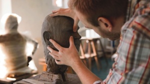Escultor trabalhando em uma escultura de barro de uma cabeça humana.