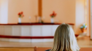 Uma mulher num banco de uma igreja olhando para o altar e a cruz.