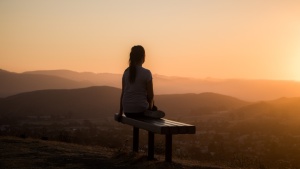 Uma mulher sentada em um banco observando o pôr do sol.