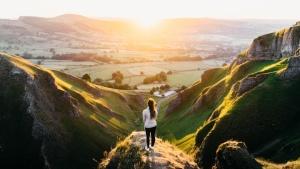 Uma mulher parada numa colina observando o nascer do sol.