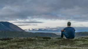 Um jovem sentado na grama olhando para as montanhas.