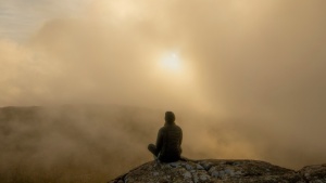 Uma pessoa sentada em uma pedra no meio da neblina matinal.
