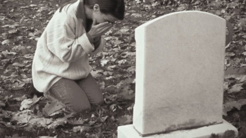 Uma mulher chorando perto de uma lápide.