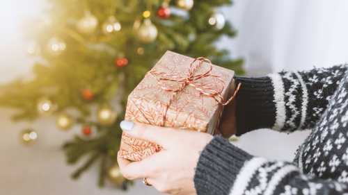 Uma pessoa segurando um presente embrulhado na frente de uma árvore de Natal.