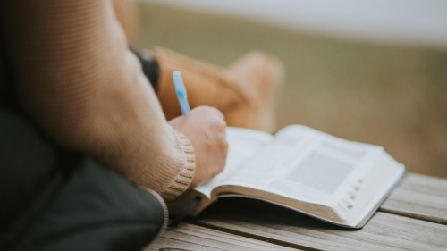 A person writing notes in a Bible.