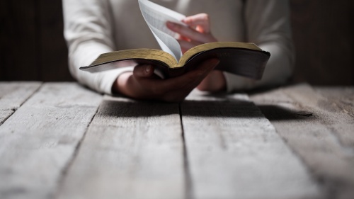 Uma pessoa sentada à mesa e lendo uma Bíblia.