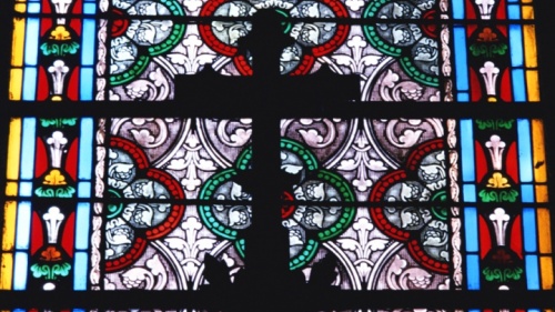 Uma cruz e um vitral dentro de uma grande igreja.
