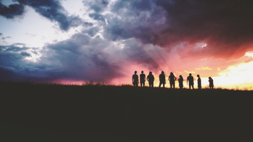A group of people standing on top of a hill with the sun setting in the background.