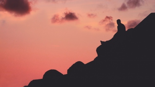 Uma pessoa sentada numa colina com o céu vermelho.