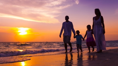 Uma família de quatro pessoas passeando na praia ao pôr do sol.