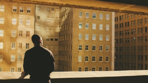 Uma pessoa olhando por cima duma parede para edifícios numa cidade.