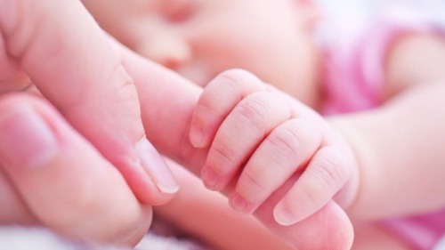 Um bebê segurando os dedos da mãe.