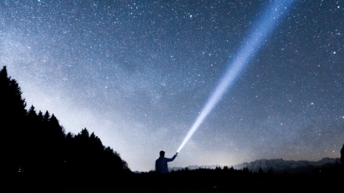 Uma pessoa apontando uma lanterna para o céu noturno.