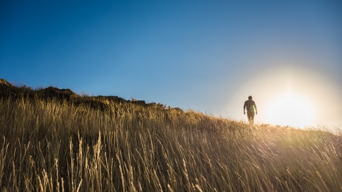 Um homem subindo uma colina gramada com o sol forte ao fundo.