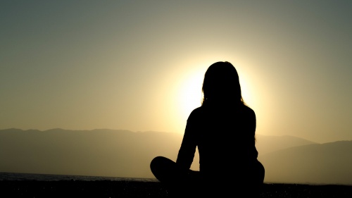 Uma mulher sentada no chão observa o pôr do sol.
