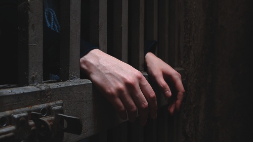 Uma pessoa atrás das grades da porta da prisão.
