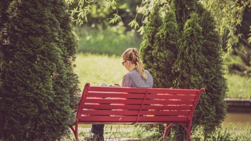 Uma mulher lendo enquanto está sentada num banco vermelho.
