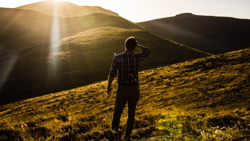 Um homem olhando para uma vista de colinas com o sol nos olhos.