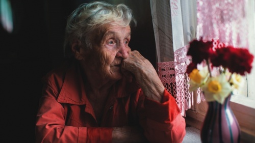 Uma senhora idosa sentada perto duma janela, olhando para fora.