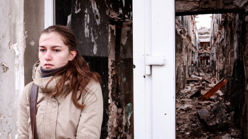 A young woman standing outside a crumbling building.