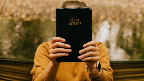 Uma mulher segurando uma Bíblia na frente do rosto. 