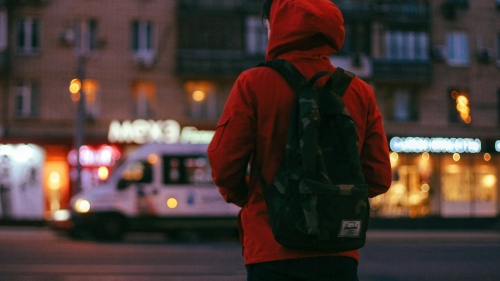 Uma pessoa usando jaqueta e mochila caminhando pela cidade.