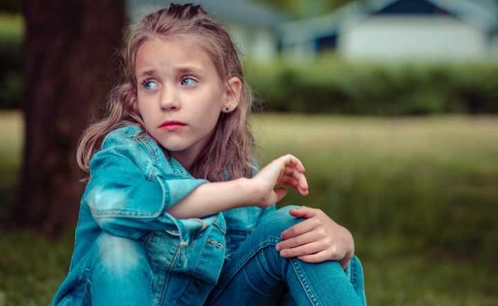 Uma garotinha com semblante triste sentada na grama.