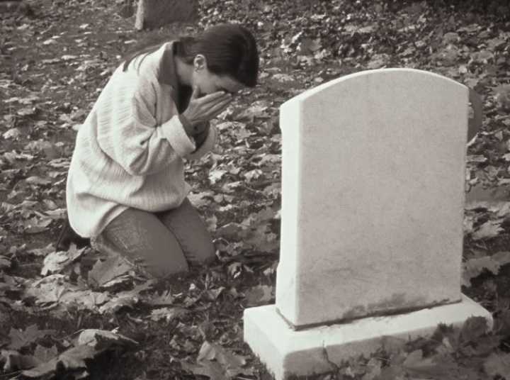Uma mulher chorando perto de uma lápide.