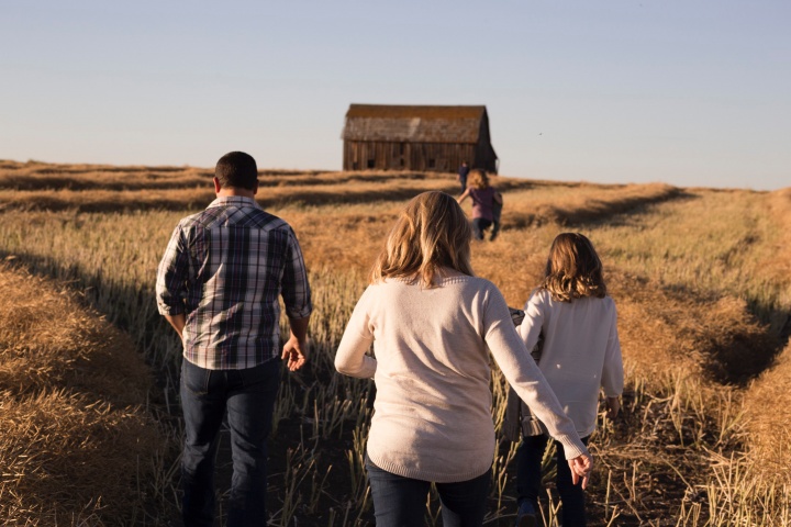 Uma família num campo de trigo caminhando para um velho celeiro.