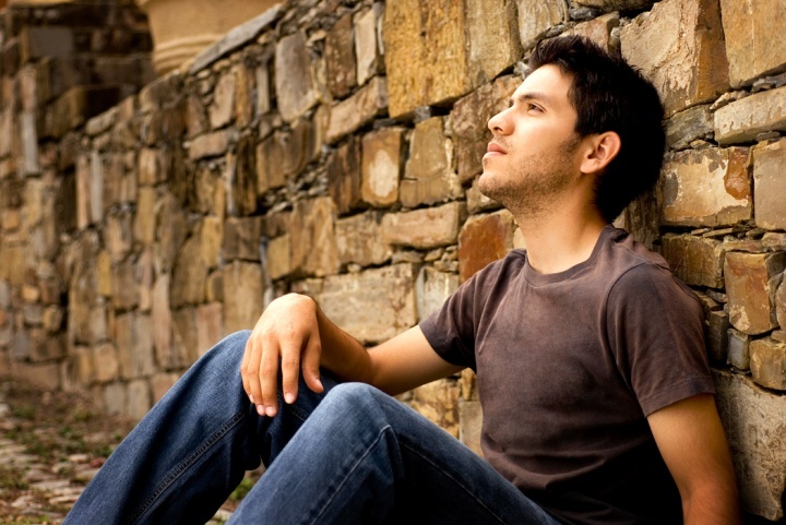 Um jovem sentado e encostado em um muro de pedra.
