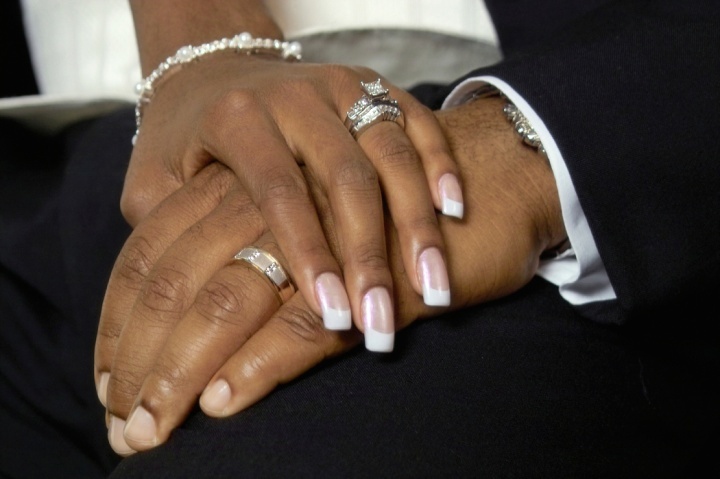 Um casal de mãos dadas mostrando suas alianças de casamento.