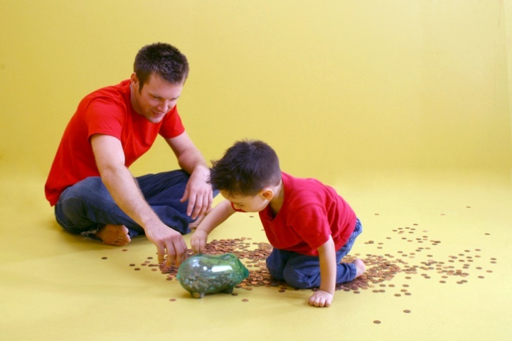 Pai e filho contando moedas de um cofrinho de vidro.