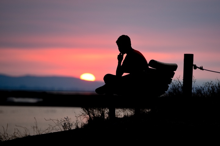 Uma pessoa sentada em um banco vendo o pôr do sol.