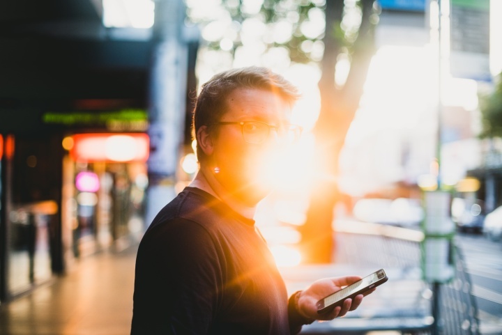 Um homem que segura um telemóvel com o sol brilhando atrás dele.