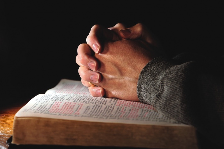 Mãos entrelaçadas em cima de uma Bíblia aberta.