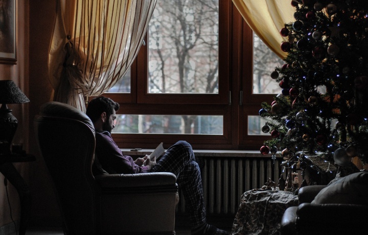 Um homem sentado em uma cadeira em frente a uma árvore de Natal.