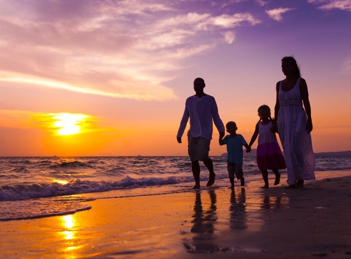 Uma família de quatro pessoas passeando na praia ao pôr do sol.