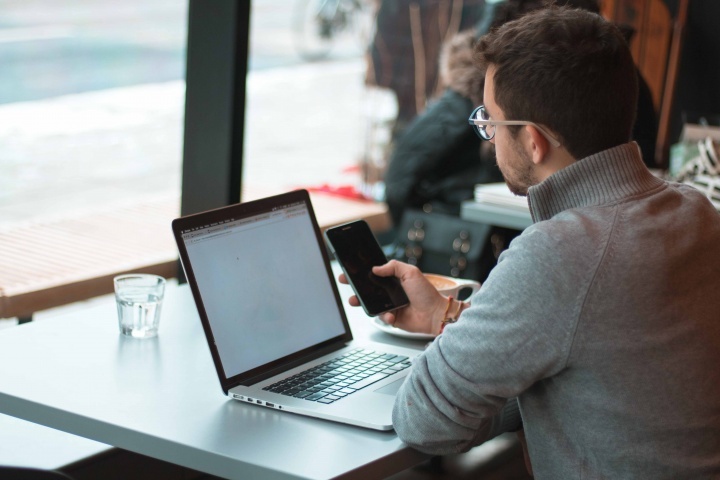 Um homem que usa seu portátil e telemóvel enquanto está num café.
