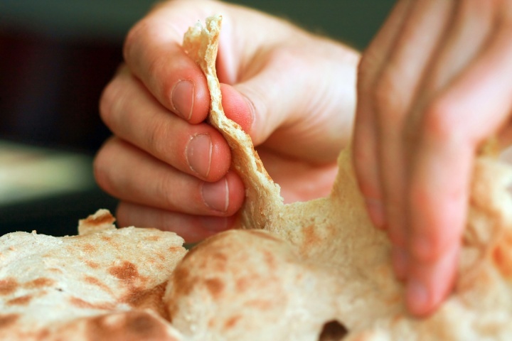 Quando você entende o pleno significado do pão, você entenderá as intenções mais profundas e amorosas de Deus para com a humanidade. Uma mão partindo pão asmo.