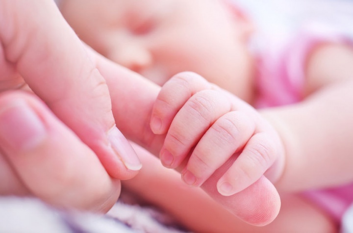 Um bebê segurando os dedos da mãe.
