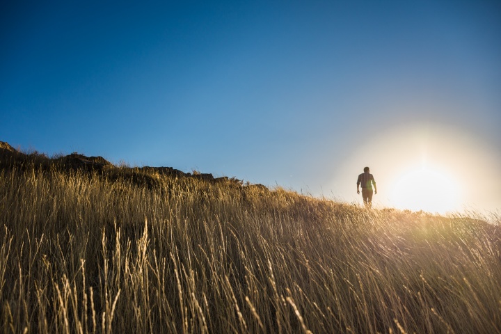 Um homem subindo uma colina gramada com o sol forte ao fundo.