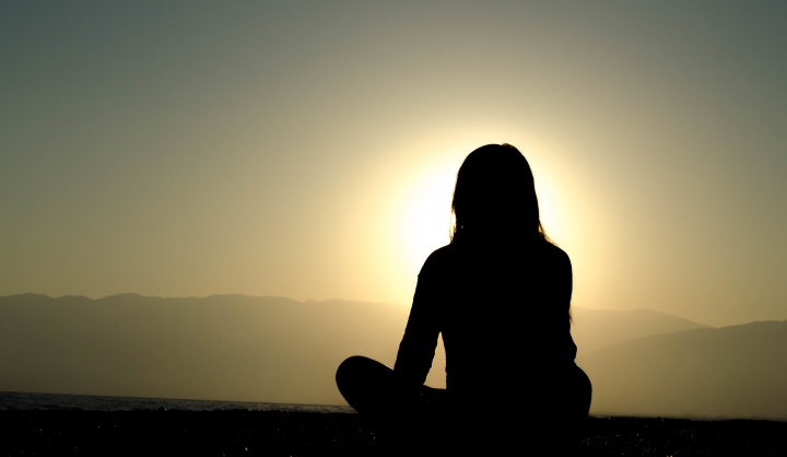 Uma mulher sentada no chão observa o pôr do sol.