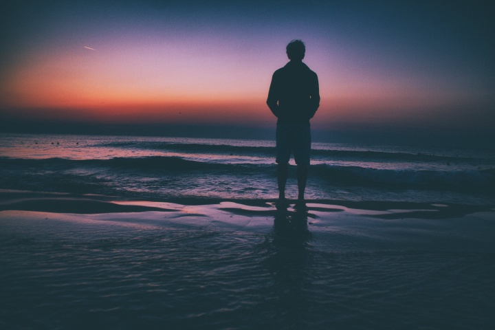 Um homem à beira de um lago ao pôr do sol.