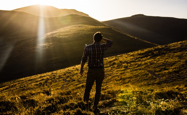 Um homem olhando para uma vista de colinas com o sol nos olhos.